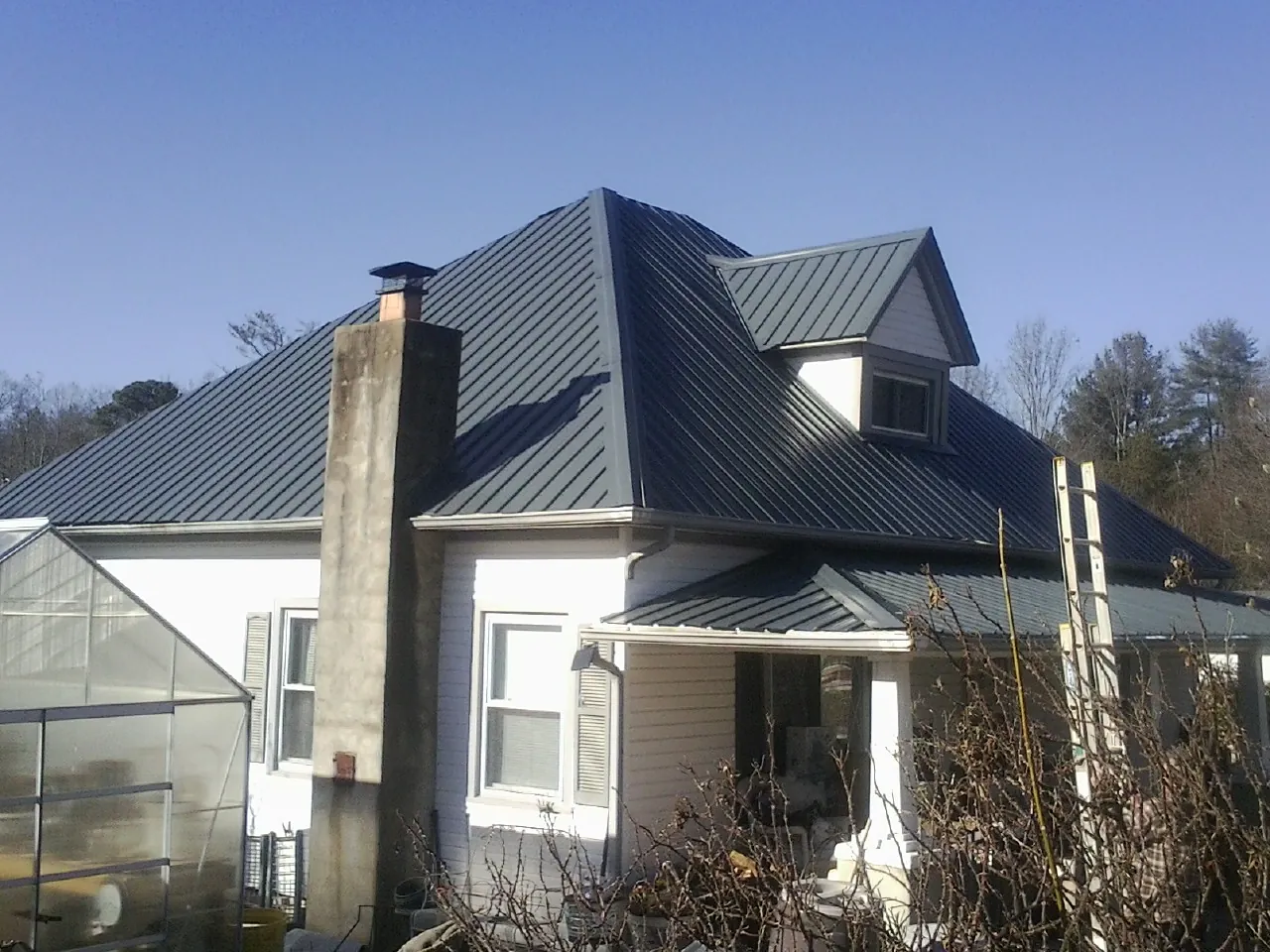 Dark blue standing seam metal roof on a white farmhouse with dormer — Slate & Tile Roof Repair by Roofing Brothers in Danielsville
