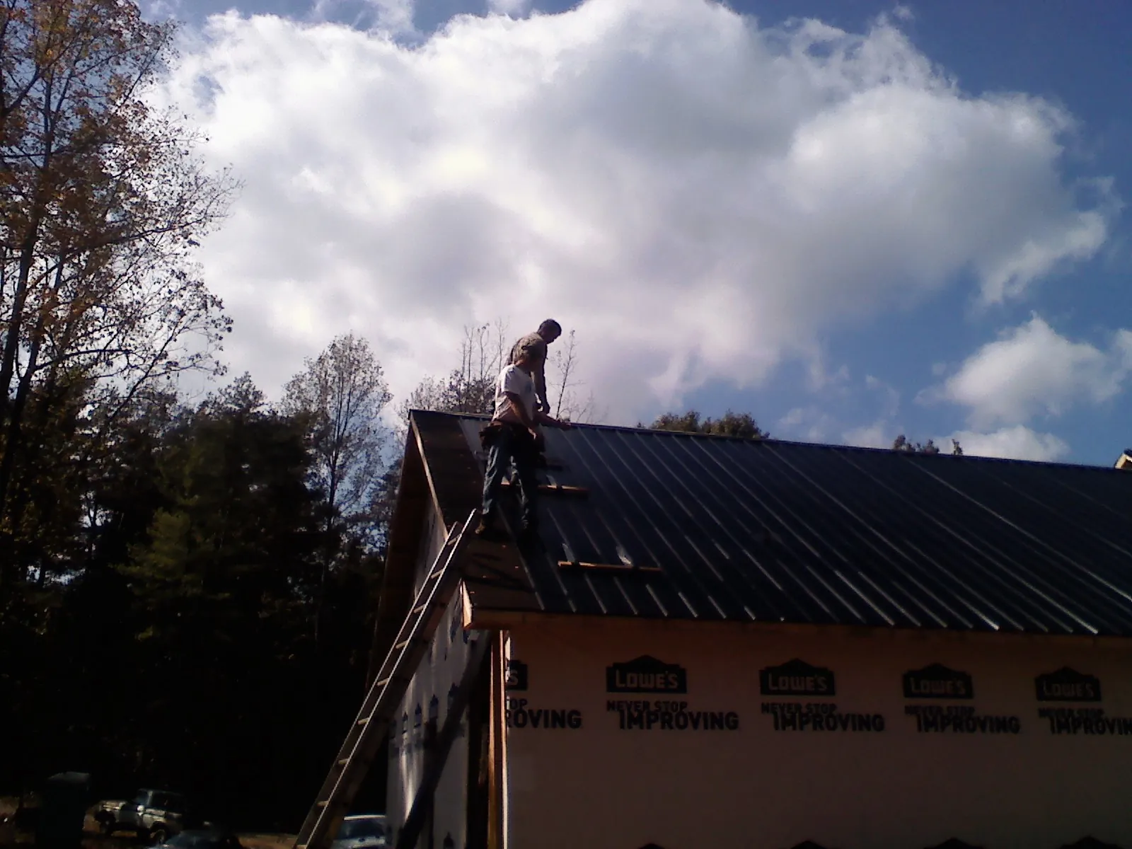 Roofer fastening dark metal panels high against a cloudy sky, from a Roof Inspection job in Danielsville