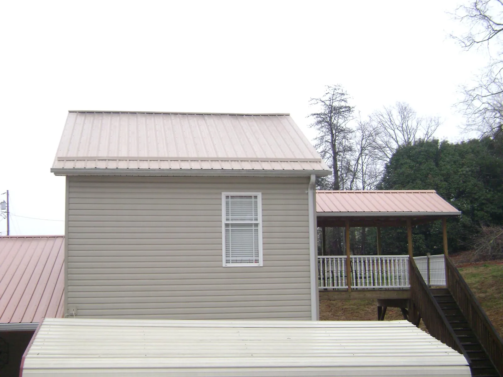 Tan metal roofs on a two story addition and attached porch, from a Roof Replacement job in Danielsville